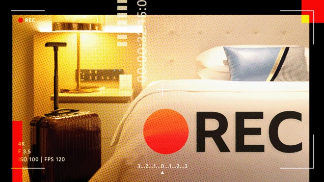 Une image représentant une chambre d'hôtel générique, une valise à roulettes noire, un lampadaire, un lit double avec un couvre-lit blanc et des oreillers à carreaux bleus, dorés, noirs et blancs, ainsi que les mots « REC » avec un point rouge symbolisant l'enregistrement inscrit en haut de l'image.
